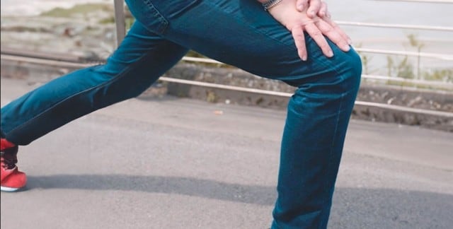Person dehnt ihr Bein in blauer Joggerjeans auf einer Straße.