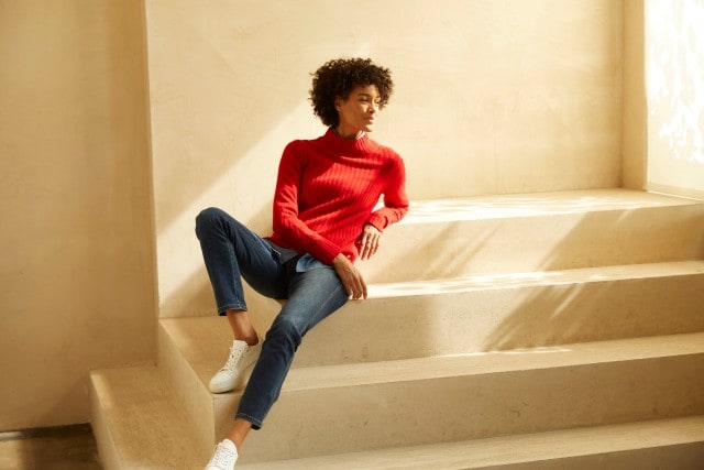 Frau sitz glücklich auf einer Treppe in ihrem roten Cashmere-Pullover