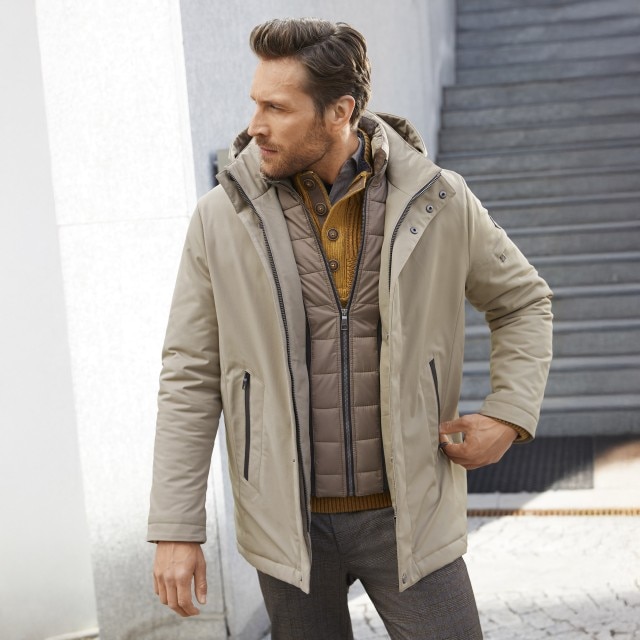 Ein Herr mit einer beigen Walbusch Jacke steht und schaut zur Seite.