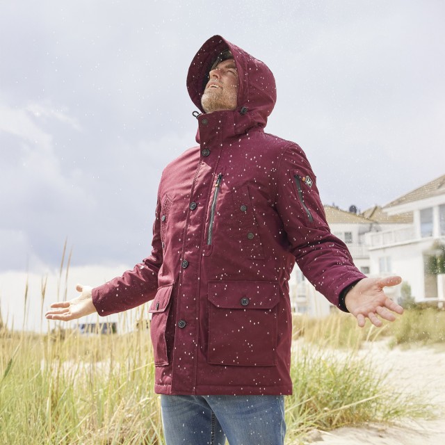 Mann in einer Wasserdichten Jacke steht in Regen und freut sich.