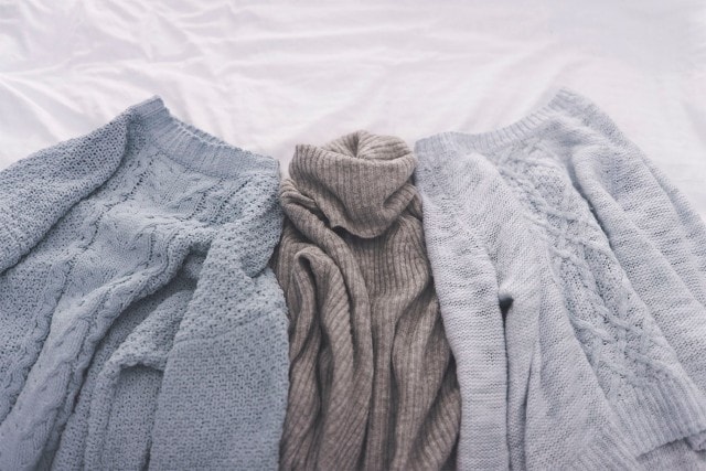 Drei Pullover, die zum Trocknen auf einem Bett liegen.
