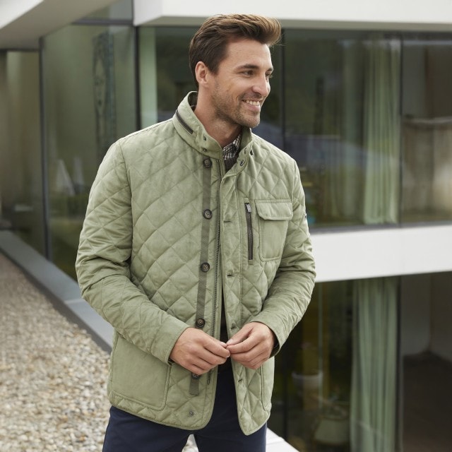 Glücklicher Mann mit einer khaki farbenden Steppjacke.