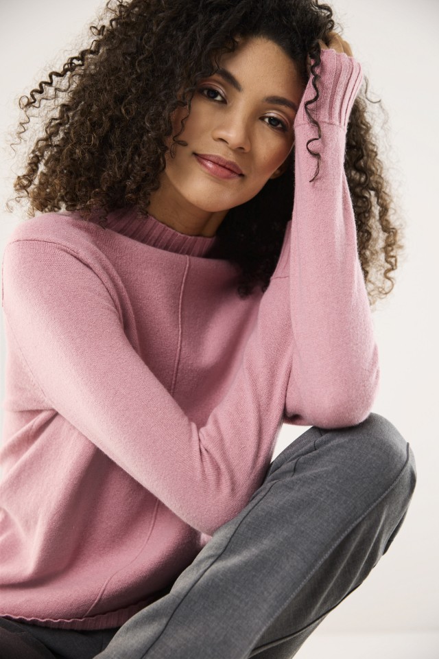 Eine sitzende Dame mit rosa Cashmere Pullover und grauer Hose 
