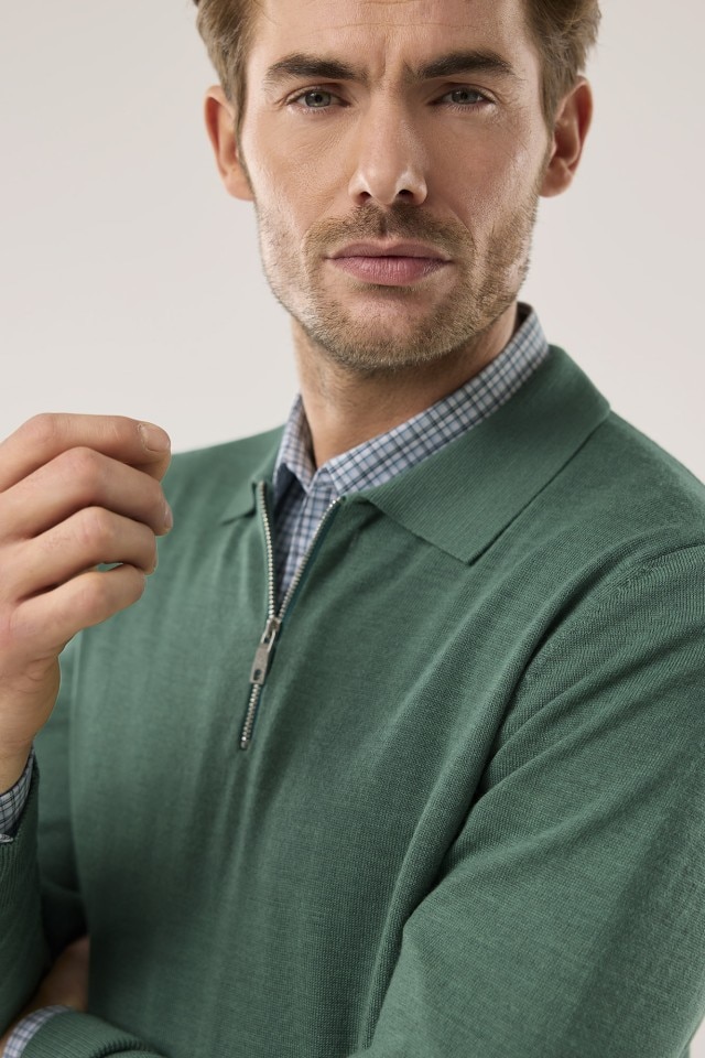 Mann in einem grünen Merino Pullover und einem Hemd drunter schaut in die Kamera