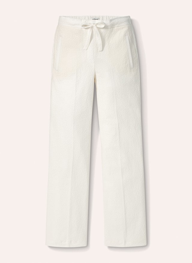 Eine weiße Hose mit geradem Bein und Tunnelzugbund liegt flach ausgebreitet vor hellem Hintergrund. Eine weiße Hose mit geradem Bein und Tunnelzugbund liegt flach ausgebreitet vor hellem Hintergrund.