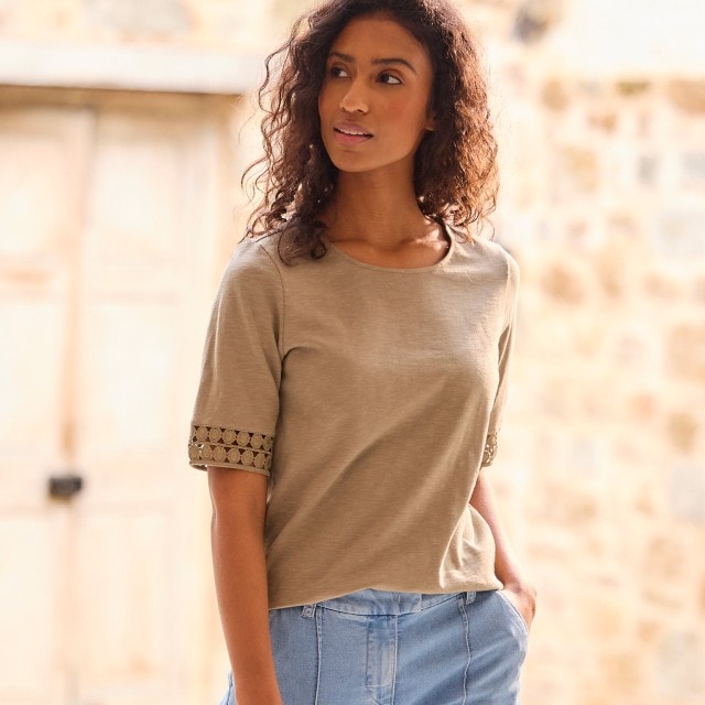 Frau in braunem Shirt und hellblauer Jeans mit einer Hand in der Hosentasche