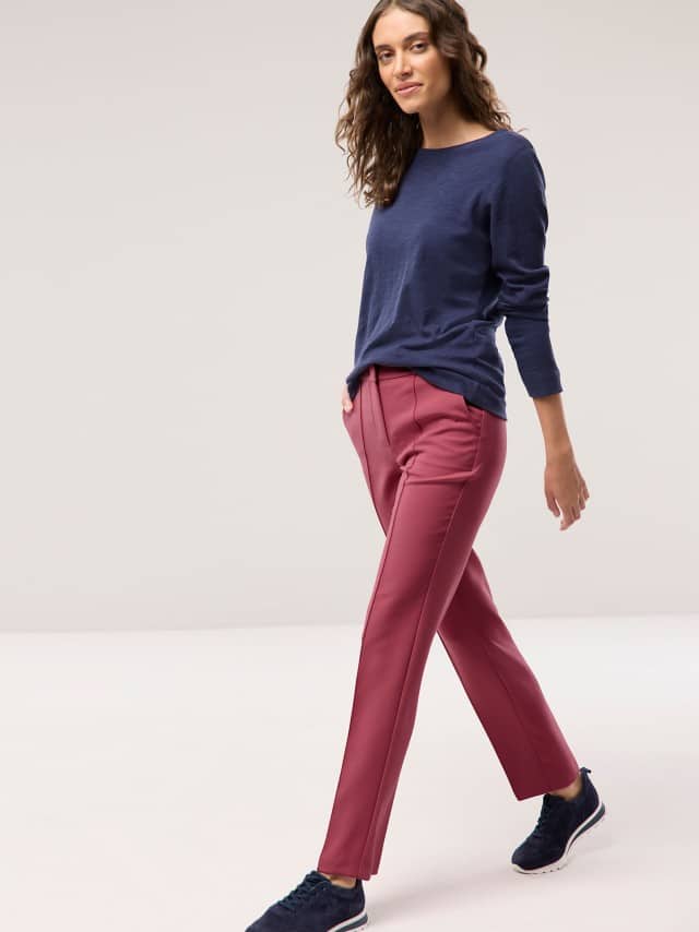 Eine Frau geht locker dahin und trägt ein dunkelblaues Langarmshirt, eine pinkrote Hose und dunkle Sneakers. Eine Frau geht locker dahin und trägt ein dunkelblaues Langarmshirt, eine pinkrote Hose und dunkle Sneakers.