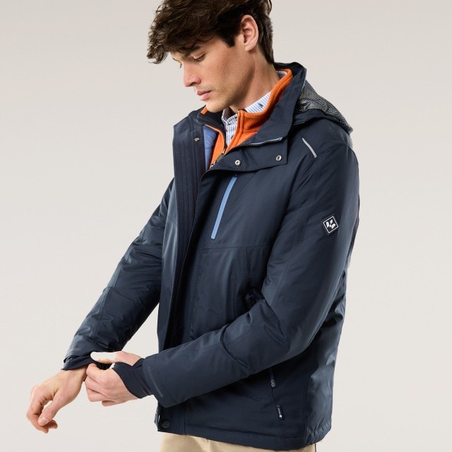 Ein Mann trägt eine blaue Jacke mit einem orangefarbenen Pullover darunter