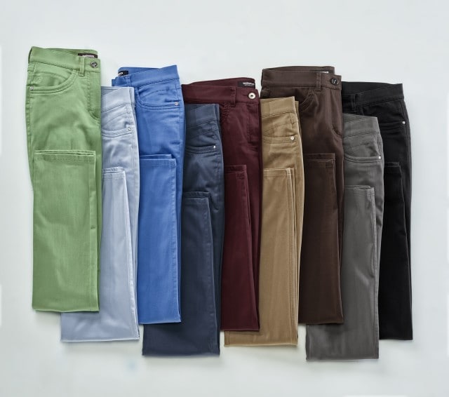 Acht Hosen in verschiedenen Farben nebeneinander angeordnet. Farben von links nach rechts: Hellgrün, Grün, Blau, Hellblau, Dunkelblau, Weinrot, Braun, Schwarz.