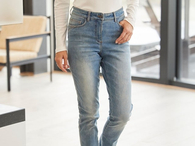 Frau trägt eine hellblaue Jeans und hat eine Hand in der Hosentasche.
