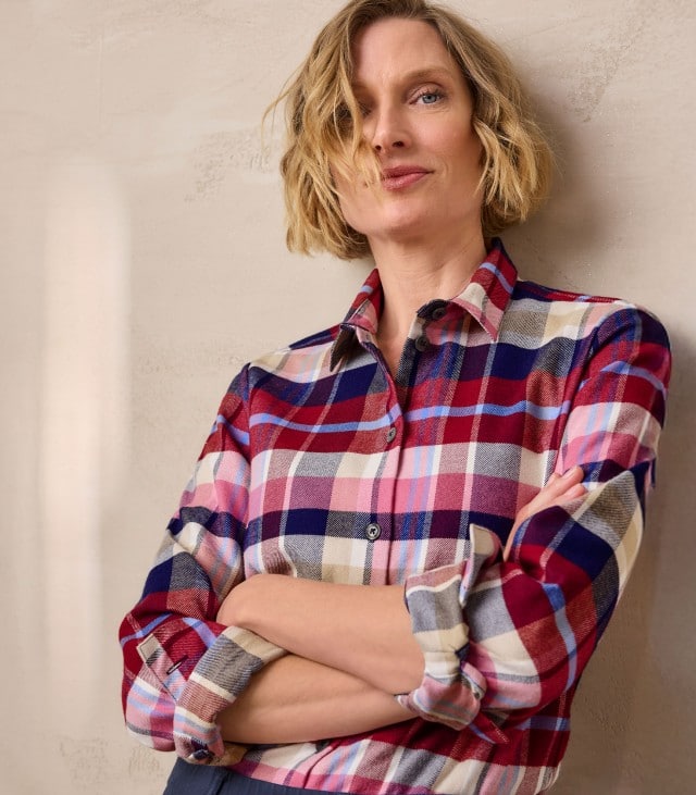 Eine Frau trägt ein kariertes Hemd in Rot-, Blau- und Beigetönen mit aufgerollten Ärmeln. Der lässige Stil wirkt modern und bequem.
