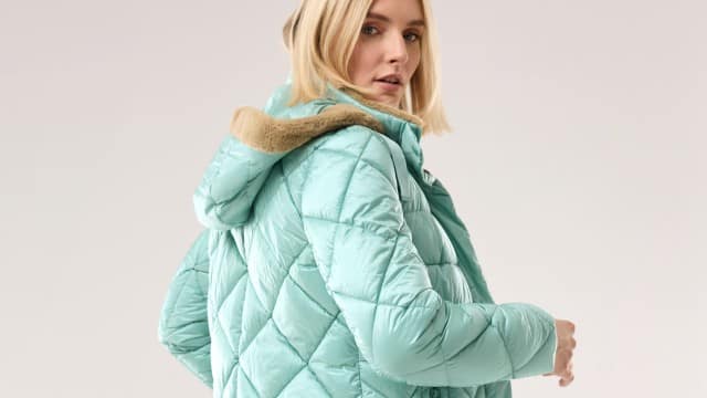 Eine Frau trägt eine mintgrüne, gesteppte Winterjacke mit Kapuze und beigefarbenem Futter. Der Stil wirkt modern und lässig. Eine Frau trägt eine mintgrüne, gesteppte Winterjacke mit Kapuze und beigefarbenem Futter. Der Stil wirkt modern und lässig.