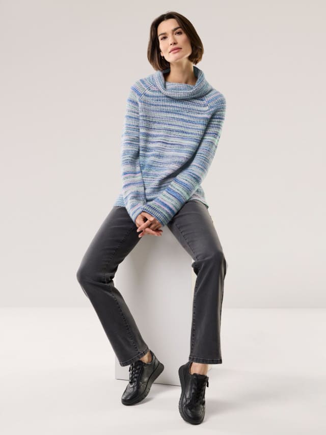 Eine Frau trägt einen gestreiften, lockeren Pullover in Blau- und Grüntönen mit weitem Kragen. Dazu kombiniert sie graue Jeans und schwarze Sneaker für einen gemütlich-modernen Look. Eine Frau trägt einen gestreiften, lockeren Pullover in Blau- und Grüntönen mit weitem Kragen. Dazu kombiniert sie graue Jeans und schwarze Sneaker für einen gemütlich-modernen Look.
