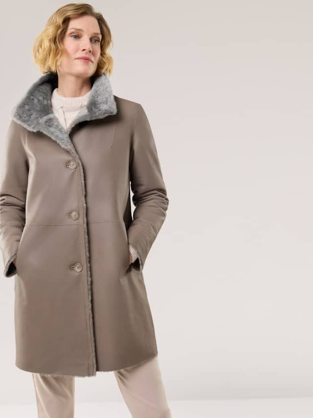 Eine Frau trägt einen knielangen, taupefarbenen Mantel mit grauem Fellkragen. Der Look ist elegant und warm, ideal für die kalte Jahreszeit. Eine Frau trägt einen knielangen, taupefarbenen Mantel mit grauem Fellkragen. Der Look ist elegant und warm, ideal für die kalte Jahreszeit.