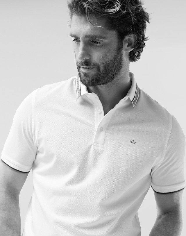 Ein Mann in einem weißen Poloshirt schaut zur Seite. 