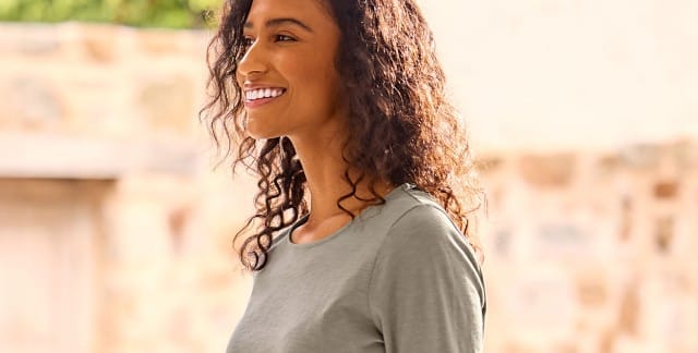 Eine Frau trägt ein schlichtes, hellgraues Langarmshirt. Das Outfit wirkt casual und bequem, passend für den Alltag.