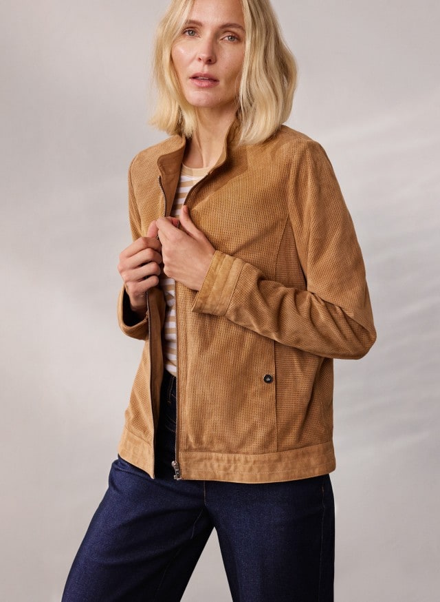 Eine Person trägt eine hellbraune Jacke über einem gestreiften Oberteil und eine dunkelblaue Jeans, während sie die Jacke mit beiden Händen hält. Eine Person trägt eine hellbraune Jacke über einem gestreiften Oberteil und eine dunkelblaue Jeans, während sie die Jacke mit beiden Händen hält.