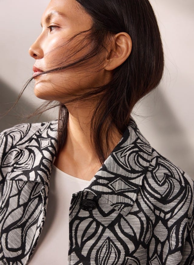 Eine Person trägt eine schwarz‑weiß gemusterte Jacke über einem weißen Oberteil und ist im Profil zu sehen. Eine Person trägt eine schwarz‑weiß gemusterte Jacke über einem weißen Oberteil und ist im Profil zu sehen.