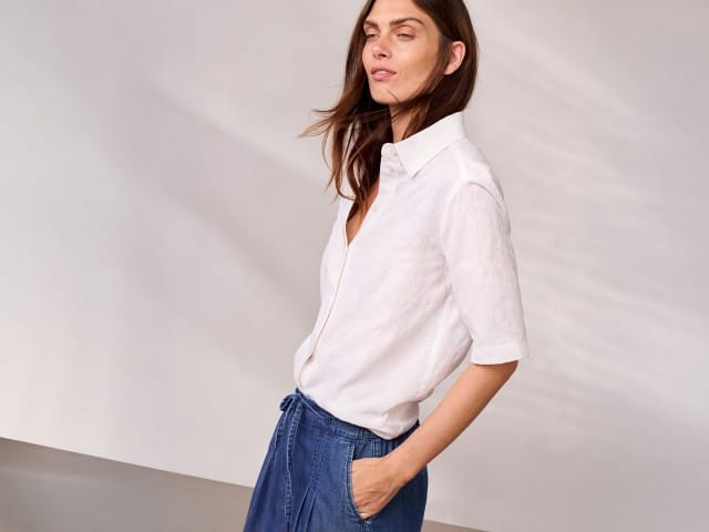 Eine Person trägt ein weißes Kurzarmhemd und blaue, knielange Hosen und blickt seitlich nach vorn. Eine Person trägt ein weißes Kurzarmhemd und blaue, knielange Hosen und blickt seitlich nach vorn.