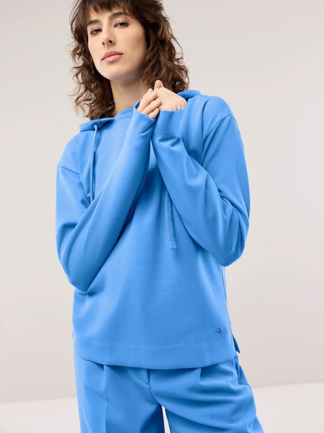 Eine Frau trägt ein blaues Hoodie‑Set, das sportlich, modern und ruhig‑lässig wirkt.
