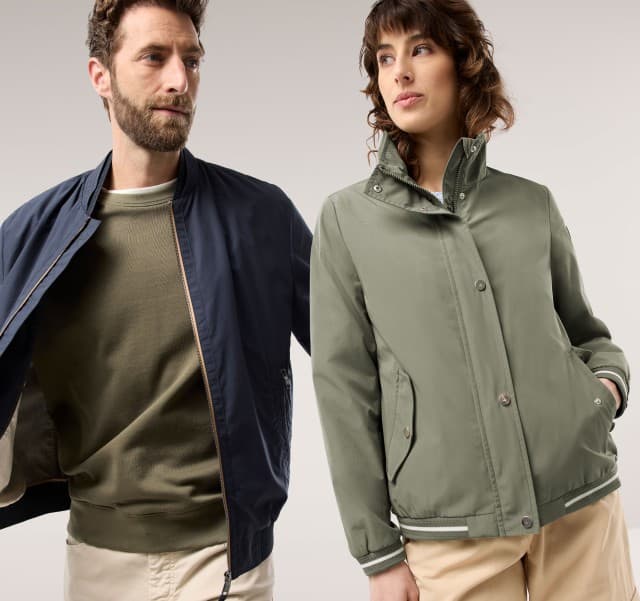 Ein Mann trägt einen Blouson in Marine, darunter ein Sweat-Shirt in Khaki, daneben Frau in der Blousonjacke Baumwollmix in Khaki.