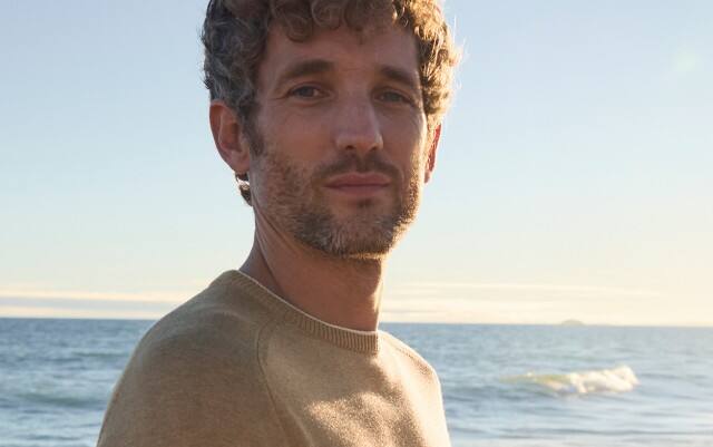 Ein Mann am Strand, trägt einen Pullover in Beige.