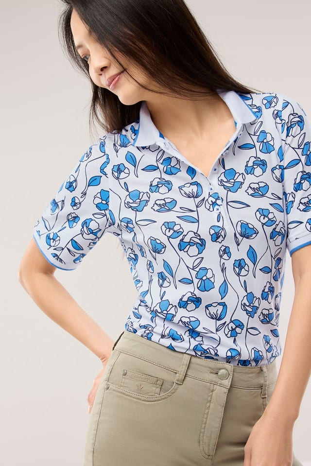 Eine Frau trägt ein Extraglatt Polo mit Blumen in Meerblau.