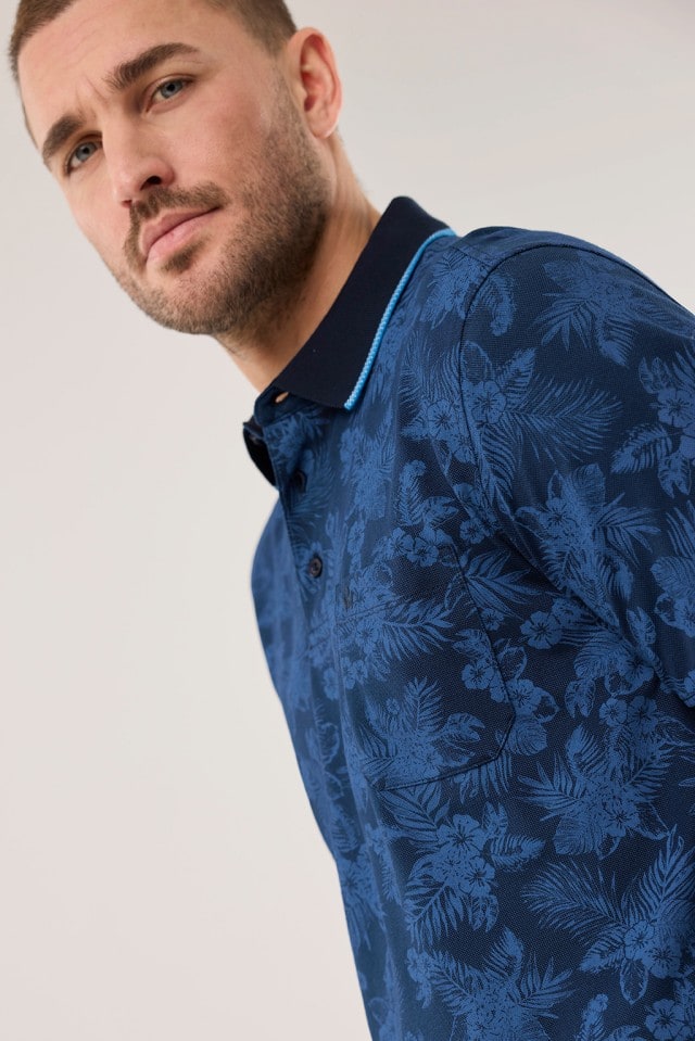 Ein Mann trägt ein blaues Extraglatt-Polo Bicolor mit Blütenmuster.