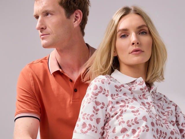 Ein Mann trägt ein Poloshirt in Orange, rechts daneben eine Frau in einem Poloshirt mit Muster Tulpenspiel in der Farbe Rosenholz.