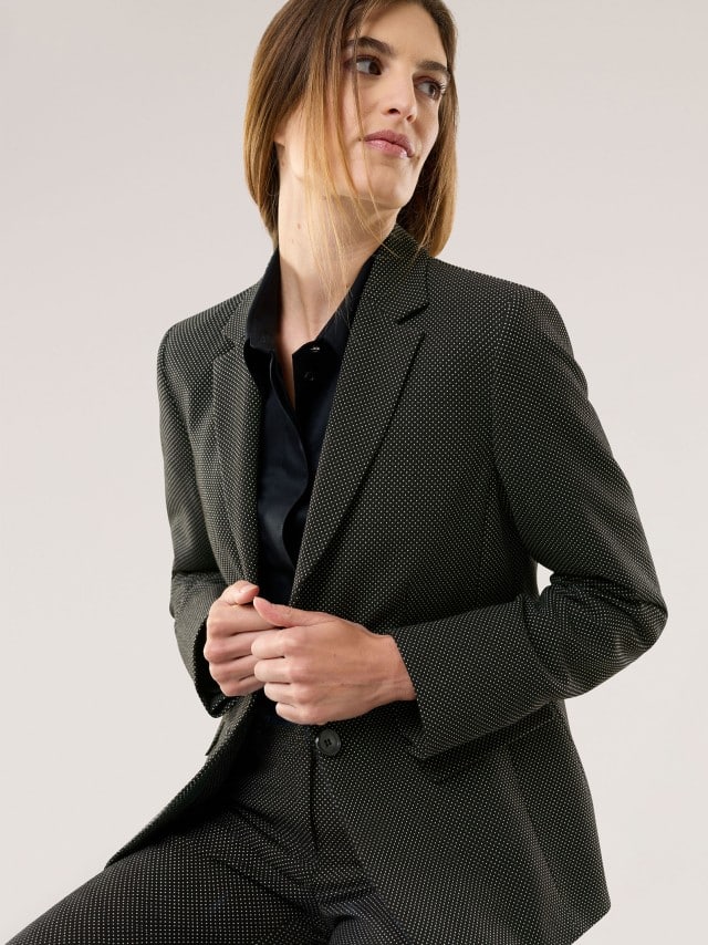 Eine Frau trägt einen feinen, dunkel strukturierten Anzug mit schwarzem Hemd, wodurch der Look stilvoll, klar und ruhig wirkt.