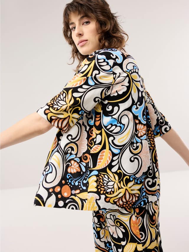 Eine Frau trägt ein farbenfroh gemustertes Oberteil mit passender Hose, wodurch der Look lebendig, verspielt und ausdrucksstark wirkt.