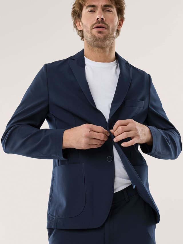 Ein Mann trägt einen dunkelblauen, modern geschnittenen Anzug über einem weißen T‑Shirt, was schlicht, zeitgemäß und entspannt wirkt.