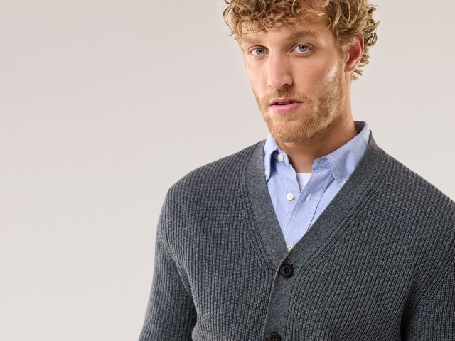 Ein Mann trägt einen dunklen Cardigan und darunter ein Hemd in Hellblau.