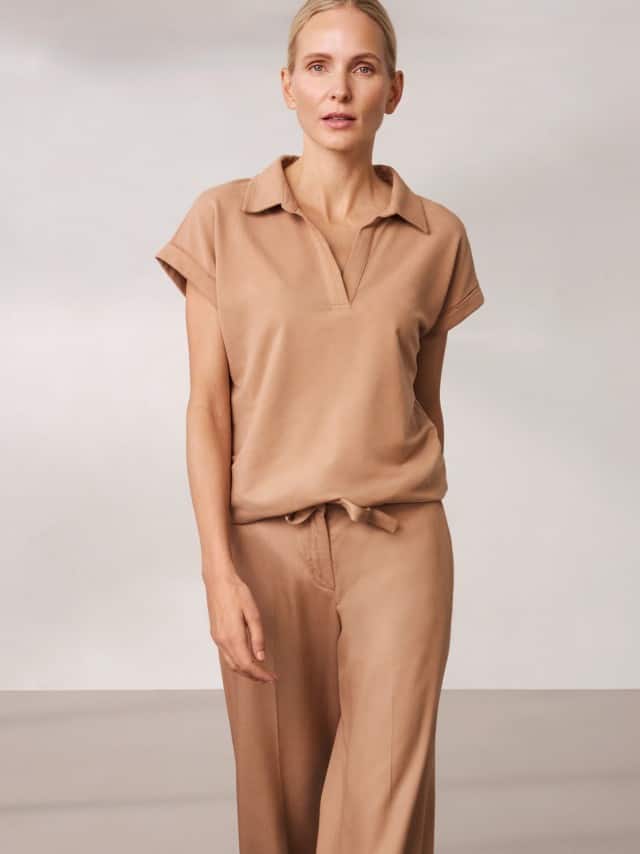 Eine Frau trägt ein beigefarbenes, locker fallendes Set aus Oberteil und Hose, das ruhig, weich und natürlich‑entspannt wirkt.