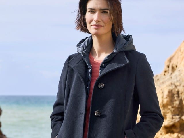 Eine Frau trägt eine Wolljacke mit Steppeinsatz in Marine, darunter ein rotes Baumwollshirt.