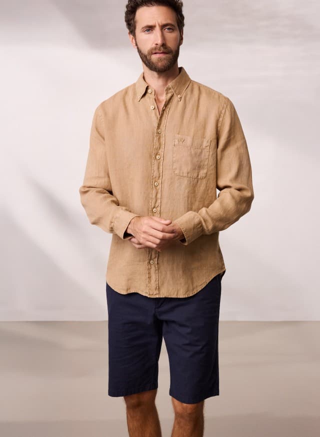 Ein Mann trägt ein Pures Leinen Hemd Überfärber in der Farbe Latte, dazu eine Bermudas.