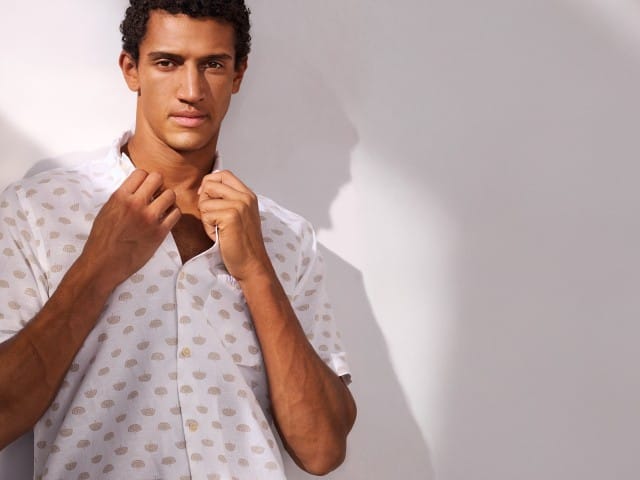 Ein Mann trägt ein Leinen-Mix Revers-Kragen-Hemd und hält den Kragen mit beiden Händen fest.