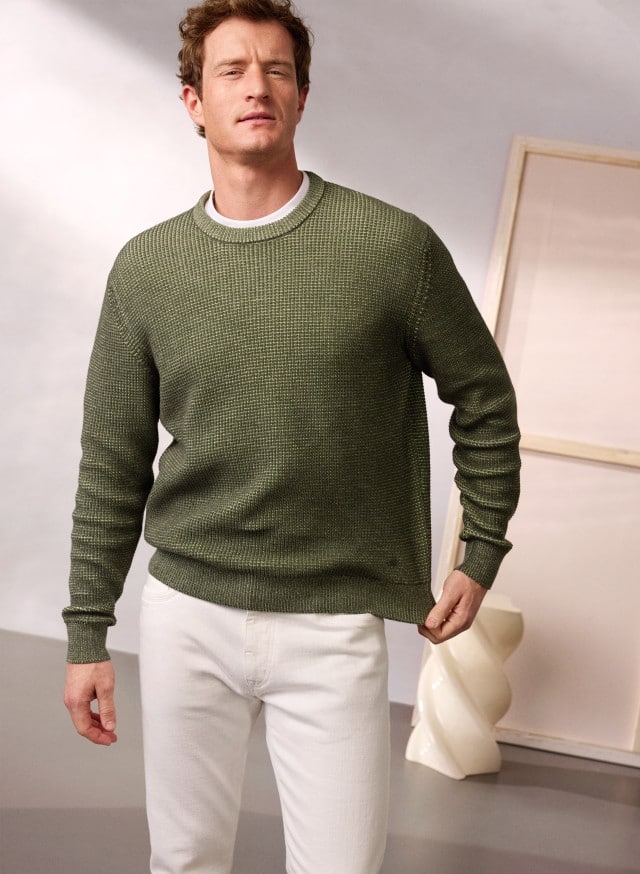 Ein Mann trägt den Strukturpullover Bicolor in Khaki, dazu eine Hose in Offwhite.
