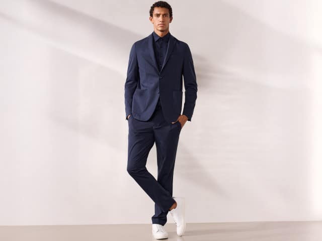 Ein Mann trägt einen Travel Anzug mit Hemd in Marine und weiße Sneaker.
