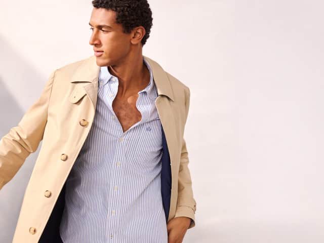 Ein Mann trägt einen Baumwoll Mantel 2 in 1 in Beige, darunter ein Hemd in hellblau.