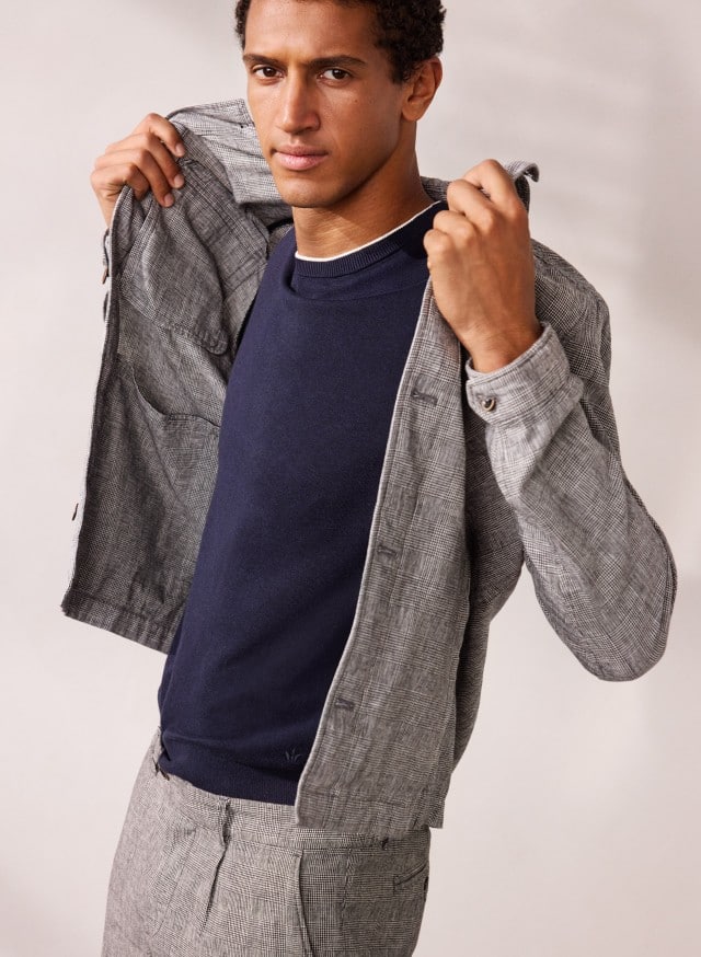 Ein Mann trägt eine Leinen Hemdjacke in Karo Schwarz, darunter ein dunkles Shirt und eine graue Hose.