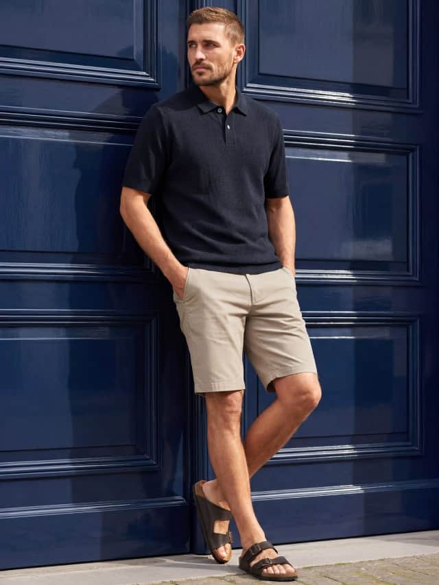Ein Mann trägt ein Strickpolo Kmastruktur in Marine, dazu Chino Shorts in Beige.