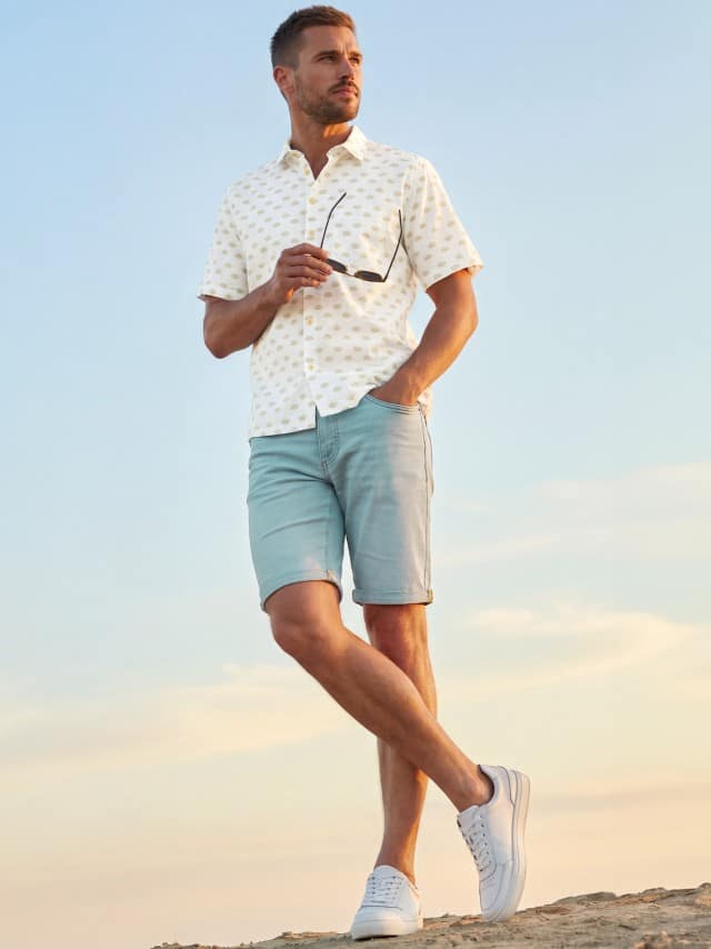 Ein Man trägt ein Leinen-Mix Revers-Kragen-Hemd in Weiß, dazu eine Jogger-Jeans Shorts.