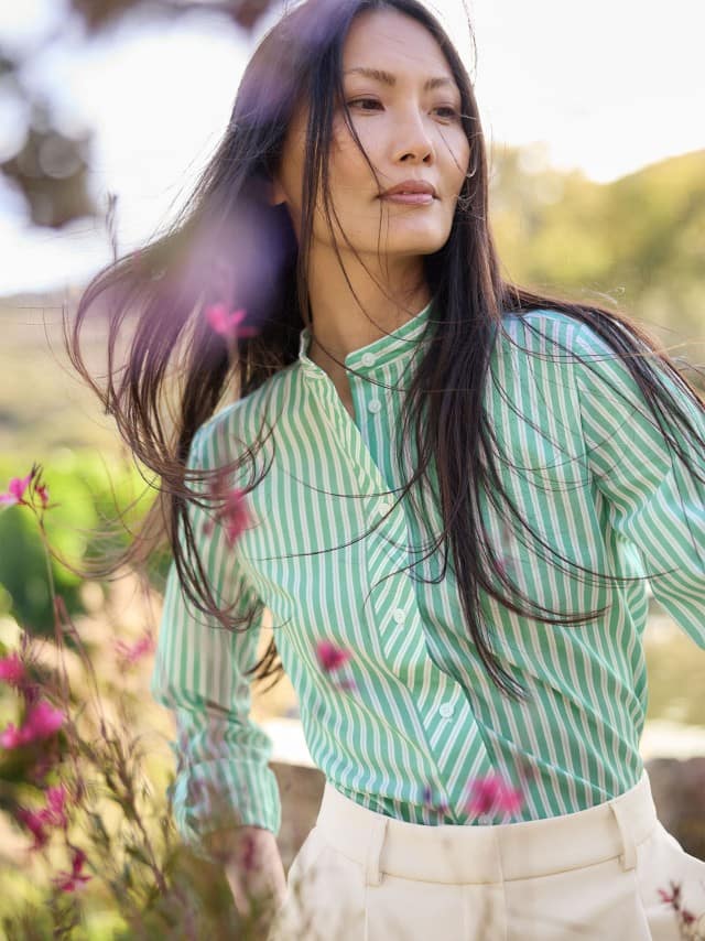 Eine Frau steht im Freien und trägt eine grün‑weiß gestreifte Bluse zu einer hellen Hose. Eine Frau steht im Freien und trägt eine grün‑weiß gestreifte Bluse zu einer hellen Hose.