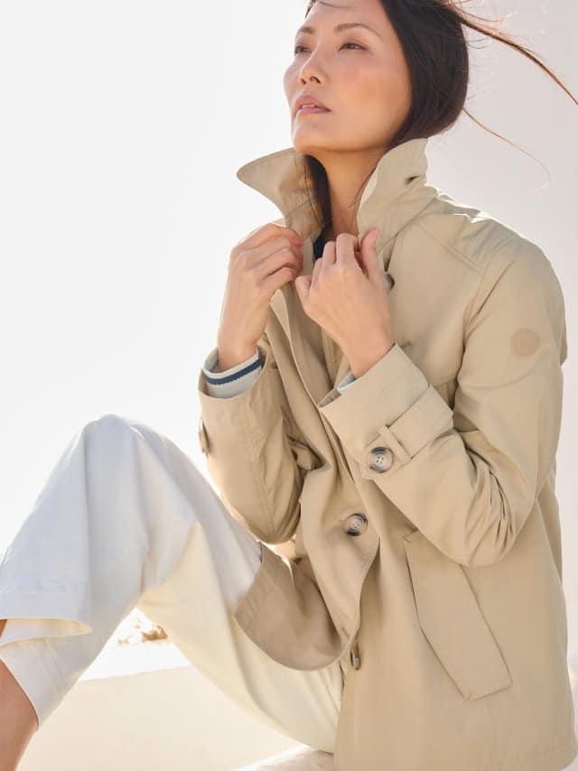 Eine Frau trägt einen hellen Trenchcoat zu einer weißen Hose, was clean, zeitlos und ruhig‑elegant wirkt. Eine Frau trägt einen hellen Trenchcoat zu einer weißen Hose, was clean, zeitlos und ruhig‑elegant wirkt.