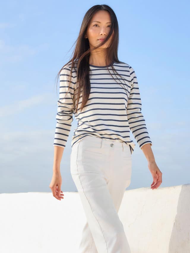 Eine Frau trägt ein weiß‑blau gestreiftes Langarmshirt zu einer weißen Hose, was frisch, maritim und entspannt wirkt. Eine Frau trägt ein weiß‑blau gestreiftes Langarmshirt zu einer weißen Hose, was frisch, maritim und entspannt wirkt.