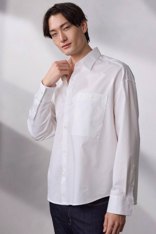 Ein Mann trägt ein weißes Hemd und steht vor einem schlichten, hellen Hintergrund.