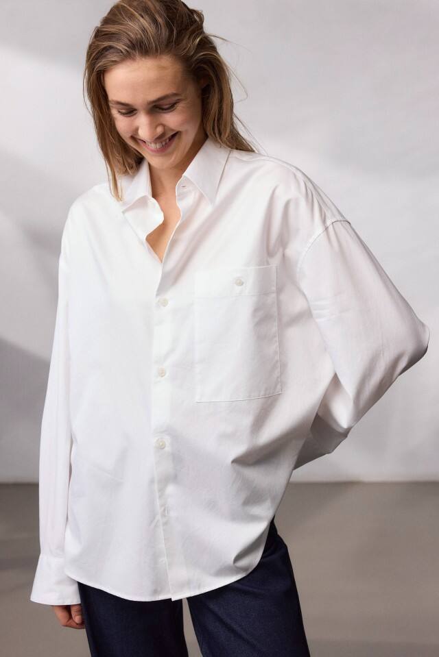 Eine Frau trägt ein weißes Hemd und blickt lächelnd nach unten.