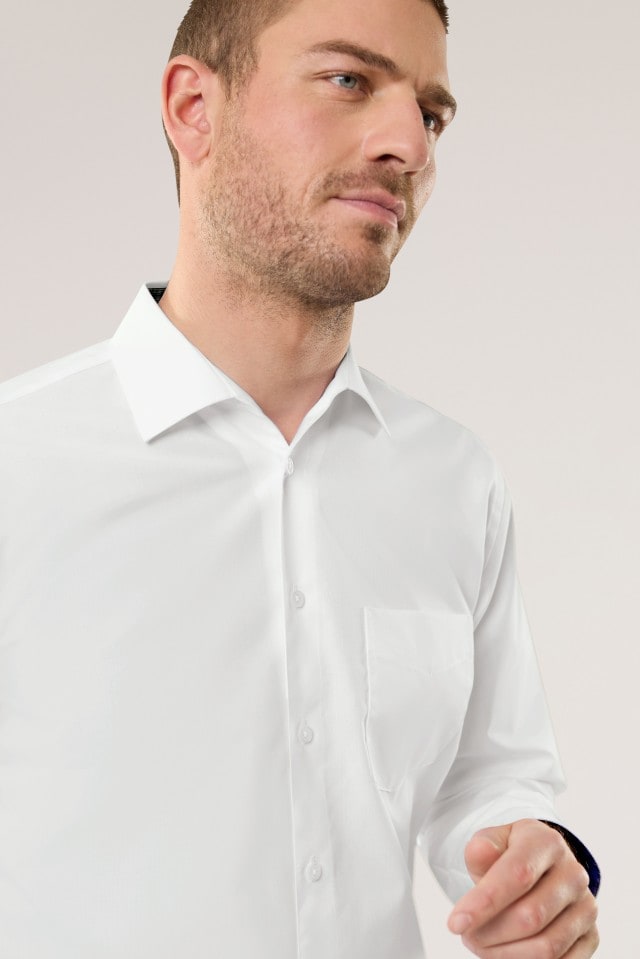 Ein Mann vor einem neutralen Hintergrund in einem weißen Hemd.