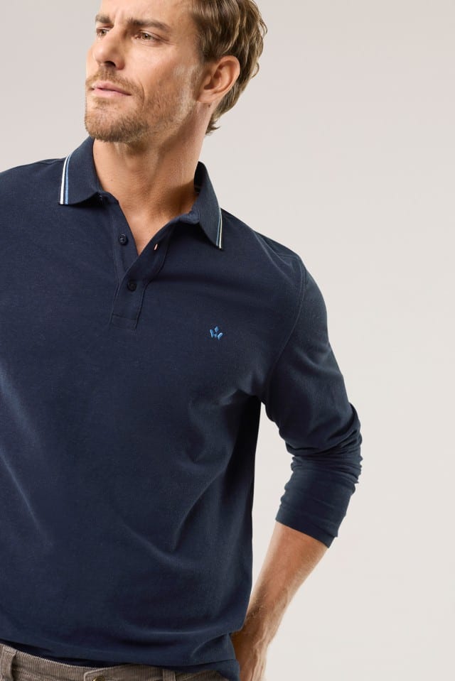 Ein Mann mit kurzem Haar und Bart trägt ein dunkelblaues, langärmliges Poloshirt mit fein gestreiftem Kragen und einer kleinen, dezenten Stickerei auf der Brust.